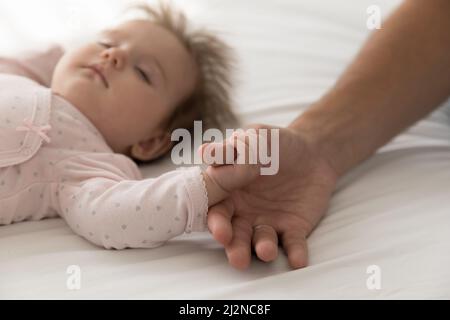 Serein adorable bébé endormi attrapant les papas pouce, tenant le doigt Banque D'Images