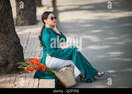 Ho Chi Minh ville, Viet Nam: Fille vietnamienne en bleu ao dai marchant dans le parc avec un bouquet de fleurs gladiolus Banque D'Images