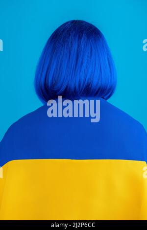 Nationalité, culture, bleu et jaune et soutenir le concept de l'Ukraine. Femme avec perruque bleue à cheveux courts et drapeau national de l'Ukraine sur les épaules debout bac Banque D'Images