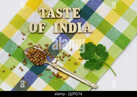 Taste of India écrit avec des lettres en bois sur un tissu à carreaux coloré avec des feuilles de coriandre fraîche et des graines de coriandre sur une cuillère vintage Banque D'Images