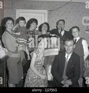 1961, historique, avec sa mère, son père et d'autres membres de la famille célébrant son anniversaire, une jeune fille s'habille, comme le signe de carton sur elle dit, comme «Lady Docker», Stockport, Manchester, Angleterre, ROYAUME-UNI. En Grande-Bretagne d'après-guerre, Lady Docker, née Norah Royce Turner dans un appartement au-dessus d'une boucherie à Derby, était une « personnalité » des médias, une socialite. Par le mariage, en particulier son troisième mariage avec Sir Bernard Docker, président de la compagnie automobile Daimler et directeur de la banque Midland, elle a mené une vie colouable et extravagante pour l'époque, mais elle n'a jamais oublié ses humbles racines de classe ouvrière. Banque D'Images