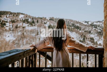 Vue arrière de la charmante jeune femme en peignoir profitant de la nature hivernale sur la grande terrasse Banque D'Images
