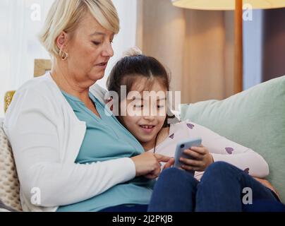 Pouvez-vous télécharger ce jeu pour moi, gran. Photo d'une petite fille utilisant un téléphone portable tout en étant assise à la maison avec sa grand-mère. Banque D'Images