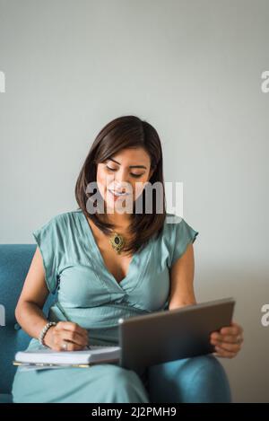 Portrait d'une femme de Latina prenant des notes dans un cours d'apprentissage à distance de la maison. Image verticale d'une femme entrant dans une classe de réception d'appel vidéo. Banque D'Images