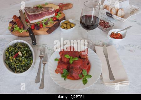 Cuisine italienne: Table avec ragoût de viande (ragù napoletano) avec basilic, brocoli, speck, salami, olives, pain, sauce chili et vin rouge. avec basilic, Banque D'Images