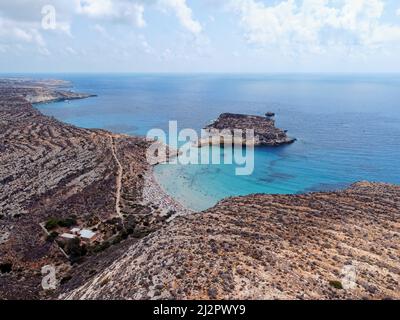 Drone aérien. Spiaggia et Isola dei Conigli, Lampedusa. Plage tranquille de style crique avec sable blanc et surf turquoise bordés de falaises rocheuses. Banque D'Images