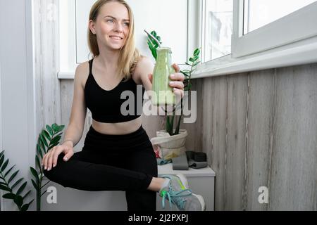 Jeune femme blonde millénelle boit du smoothie végétalien Detox. Femme faisant des exercices de yoga à la maison. Manger propre, perte de poids, alimentation saine Banque D'Images