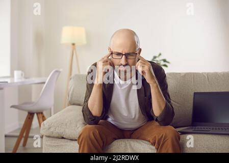 Un homme sérieux et perplexe, assis sur un canapé et pensant, essayant de répondre à une question difficile Banque D'Images