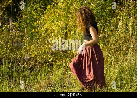 La fille marche à travers le champ. Une fille dans un bk marche parmi les plantes. La marche d'automne des filles mauries. La fille cherche son humeur dans la forêt. Banque D'Images