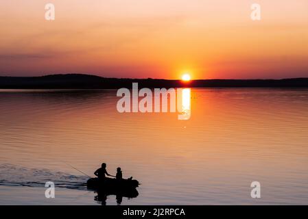 Silhouettes de pêcheurs sur un bateau revenant de la pêche dans la soirée sur le fond du soleil couchant Banque D'Images