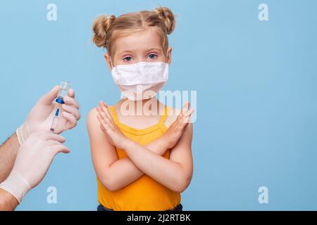 Un médecin vaccine une petite fille blonde dans un masque médical. Banque D'Images