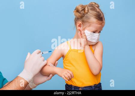 Un médecin vaccine une petite fille blonde dans un masque médical. Banque D'Images