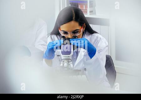 Beau jeune scientifique ou assistant de laboratoire utilisant un microscope dans l'industrie pharmaceutique de laboratoire Banque D'Images