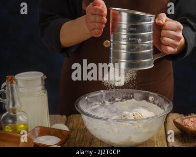 Un chef professionnel filtre la farine à travers un tamis sur un fond en bois. Gros plan. Cuisson de la pâte par le chef. Produits à base de pâte - pizza, Banque D'Images