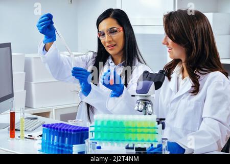 Deux belles jeunes femmes scientifiques travaillant en laboratoire avec des tubes à essai faisant de la recherche pharmaceutique Banque D'Images