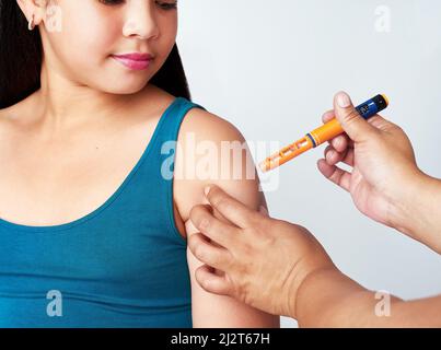 Mais tout d'abord, l'insuline. Photo studio d'une jeune fille mignonne recevant une injection d'insuline d'une femme méconnaissable sur fond gris. Banque D'Images