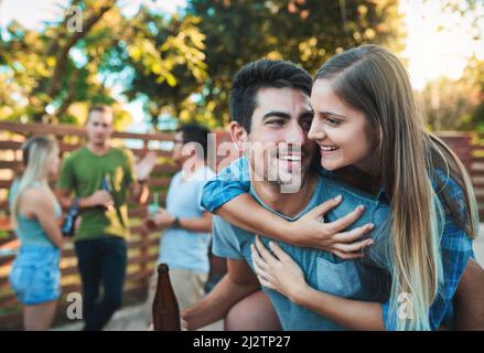 Quand votre petit ami est aussi votre meilleur ami. Photo d'un jeune couple en train de profiter d'une promenade en pigeyback tout en traînant avec leurs amis. Banque D'Images