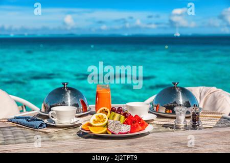 Petit déjeuner de vacances dans une chambre d'hôtel de luxe avec vue sur l'océan. Vacances romantiques en lune de miel aux Maldives ou à Tahiti. Présentation de deux assiettes, fruits Banque D'Images