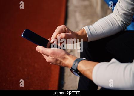 Homme dans les vêtements de sport assis sur le siège du stade et de navigation sur smartphone après l'entraînement Banque D'Images