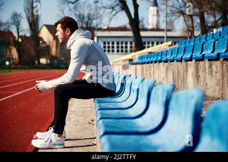 Homme dans les vêtements de sport se reposant au siège du stade après les exercices Banque D'Images