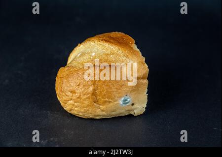 Un morceau de pain moldy sur fond noir. Un morceau de pain de blé rassis. Banque D'Images