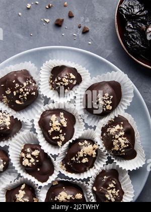 Bonbons au chocolat végétalien cru faits maison sans sucre, avec prunes séchées et noix sur fond bleu plat Banque D'Images