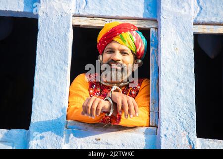 Un Indien heureux portant une tenue traditionnelle colorée rajasthani et turban regardant par la fenêtre., Inde rurale. Banque D'Images