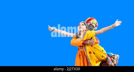 Joyeux père indien ascenseur fille portant le traditionnel coloré rajasthani tenue jouant ensemble ayant amusant isolé sur fond bleu. Espace de copie Banque D'Images