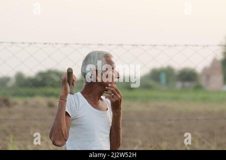 Photo en gros plan d'un agriculteur indien âgé qui pense à quelque chose en tenant une pelle dans la main au coucher du soleil Banque D'Images