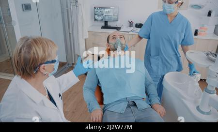 Équipe de spécialistes en anesthésie sur le patient dans le bureau de la dentisterie. Infirmière appliquant le masque d'oxygène sur le visage, donnant anesthésiant à l'homme avant de commencer la procédure stomatologique dans l'armoire. Banque D'Images