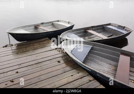 Trois petites lignes de bateaux amarrés à la jetée en bois sur le lac STILL en un jour de pluie Banque D'Images