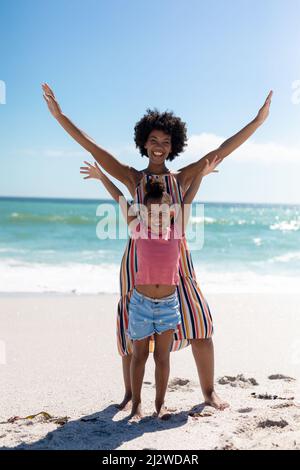 Portrait complet de la mère et de la fille afro-américaines heureuses avec les bras levés à la plage Banque D'Images