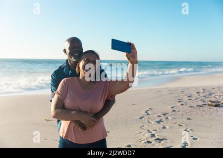 Bonne femme afro-américaine prenant selfie avec l'homme depuis un smartphone à la plage Banque D'Images