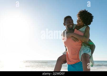 Homme afro-américain donnant le pigeyback à la petite amie à la plage contre le ciel avec l'espace de copie Banque D'Images