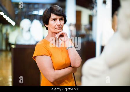 Femme d'âge moyen réfléchie examinant l'exposition dans la salle de musée de la sculpture ancienne Banque D'Images