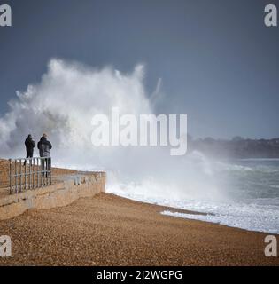Deux personnes se rapprochent de l'action en prenant des photos de vagues qui se brisent contre la position dure causée par Storm Eunice qui a frappé le Royaume-Uni en février 2022 Banque D'Images