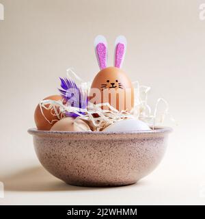 Composition de Pâques. Œufs de Pâques et œuf de lapin avec oreilles de lapin et museau dans un bol de foin sur fond pastel. Banque D'Images