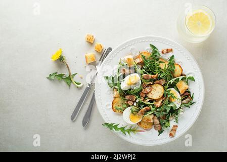 Salade de pissenlits avec œufs, pommes de terre, bacon et croûtons sur fond gris Banque D'Images