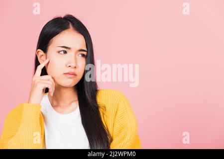 Portrait asiatique belle jeune femme debout menton poignée détendue penser à quelque chose à la question studio tourné isolé sur fond rose, Banque D'Images
