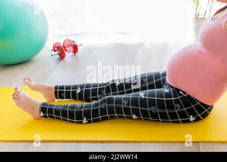 jeune femme enceinte assise sur un tapis d'exercice avec ses jambes étirées faisant des exercices et des étirements pendant la grossesse Banque D'Images