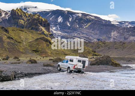 Campeurs fording d'une petite rivière dans les montagnes islandaises Banque D'Images