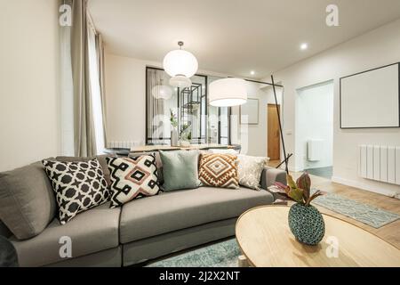 canapé trois places dans un salon avec tables en bois avec différentes lampes, radiateurs en aluminium blanc et mur en verre avec cadres en métal Banque D'Images