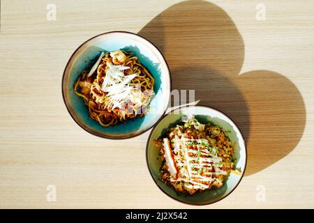 Vue de dessus minimale sur deux bols avec de délicieux plats asiatiques sur une table en bois à la lumière du soleil avec des ombres élevées, espace de copie Banque D'Images