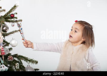 Une petite fille a pris le temps de prendre un chocolat au loin de l'arbre de Noël. Une personnalité tout-petit. Arrière-plan blanc avec espace de copie Banque D'Images