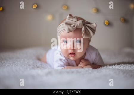 Bébé fille de 3 mois se trouve sur un lit avec des vêtements blancs sur son ventre, bébé matin, concept de substance de bébé. Banque D'Images