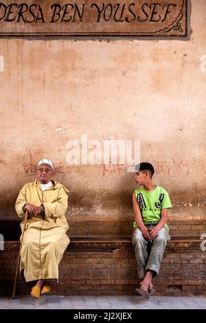 Vieux hommes dans des vêtements traditionnels djellaba et un garçon dans des vêtements de style occidental assis dans la vieille partie de la médina, Marrakech, Maroc Banque D'Images