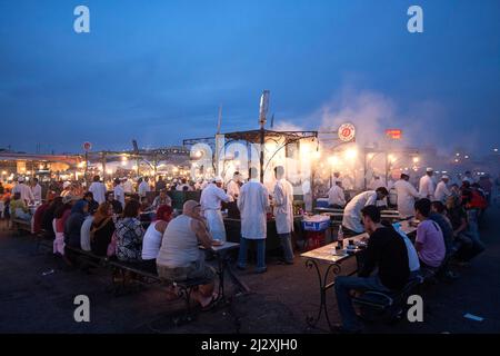 Les personnes attendant de la nourriture à la stalle alimentaire sur le marché et la place Jemaa el-Fna (Jemaa el-Fna) au crépuscule, la vieille médina, Marrakech, Maroc Banque D'Images