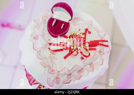 Sur une table en forme de coeur blanc magnifiquement décorée avec des fleurs se trouve boîte avec des anneaux de mariage de jeunes mariés. Banque D'Images