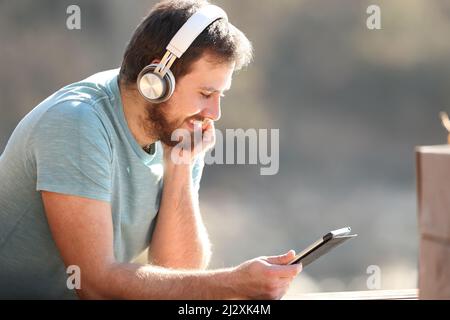 Un homme heureux avec un casque sans fil pour regarder du contenu multimédia en extérieur sur une tablette Banque D'Images