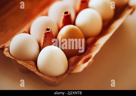 Il y a des œufs de poulet blancs dans une boîte en carton orange du magasin, mais un œuf est brun. Pas comme tout le monde. Pâques. Petit déjeuner sain. Banque D'Images